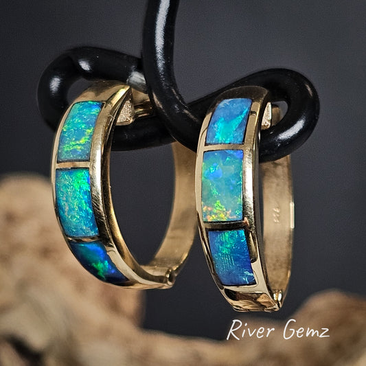Gold hoop earrings with three blue opal stones on a dark background, branded 'River Gemz'.