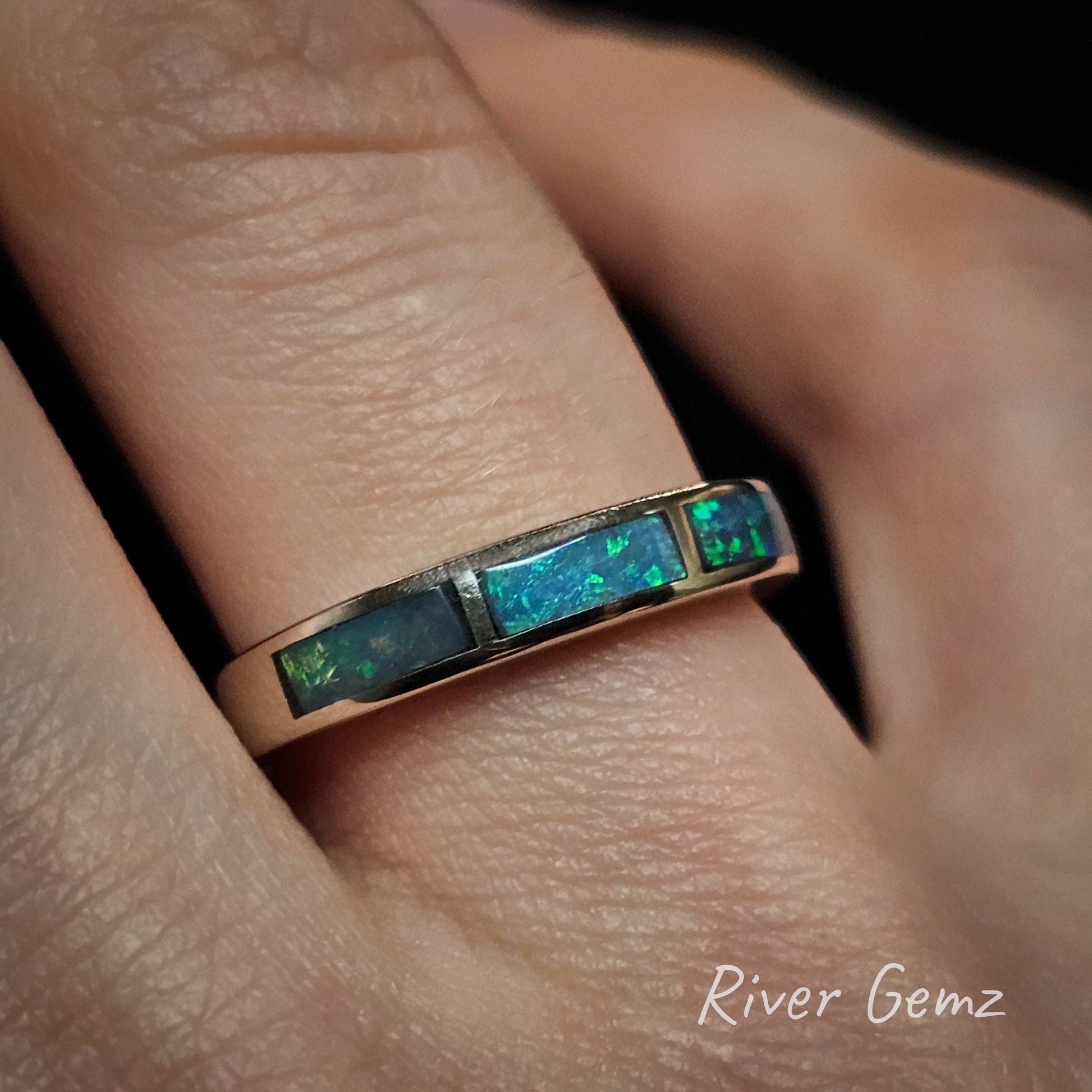 Ring with 3 channel set opal stones on a finger, branded 'River Gemz'.