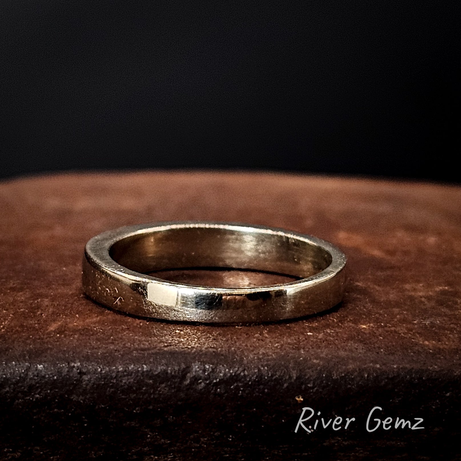 Rear view of white gold ring on a brown surface with 'River Gemz' branding.