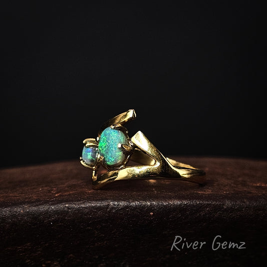 Gold ring with two blue/green opals on a dark background, branded 'River Gemz'.