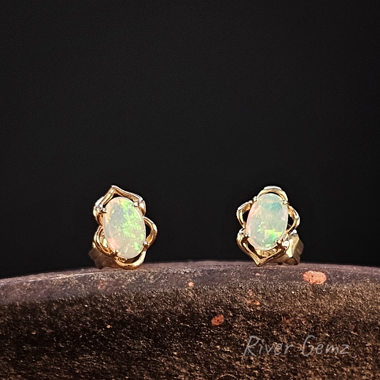 Oval shaped light opals set in yellow gold studs against a dark background.