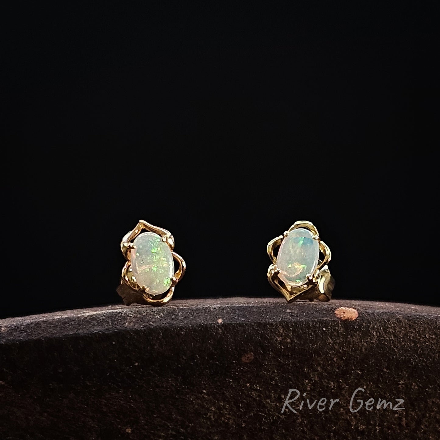Pair of opal earrings with gold settings on a dark background, branded 'River Gemz'.