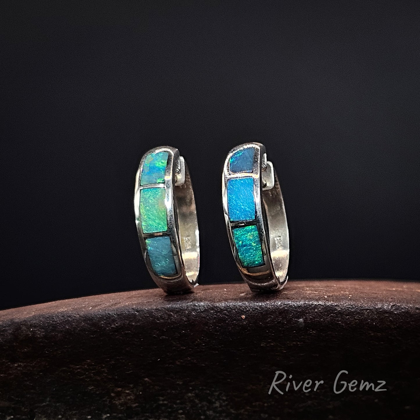 Pair of turquoise light opals inlayed in silver sleeper earrings on a dark surface with 'River Gemz' branding.