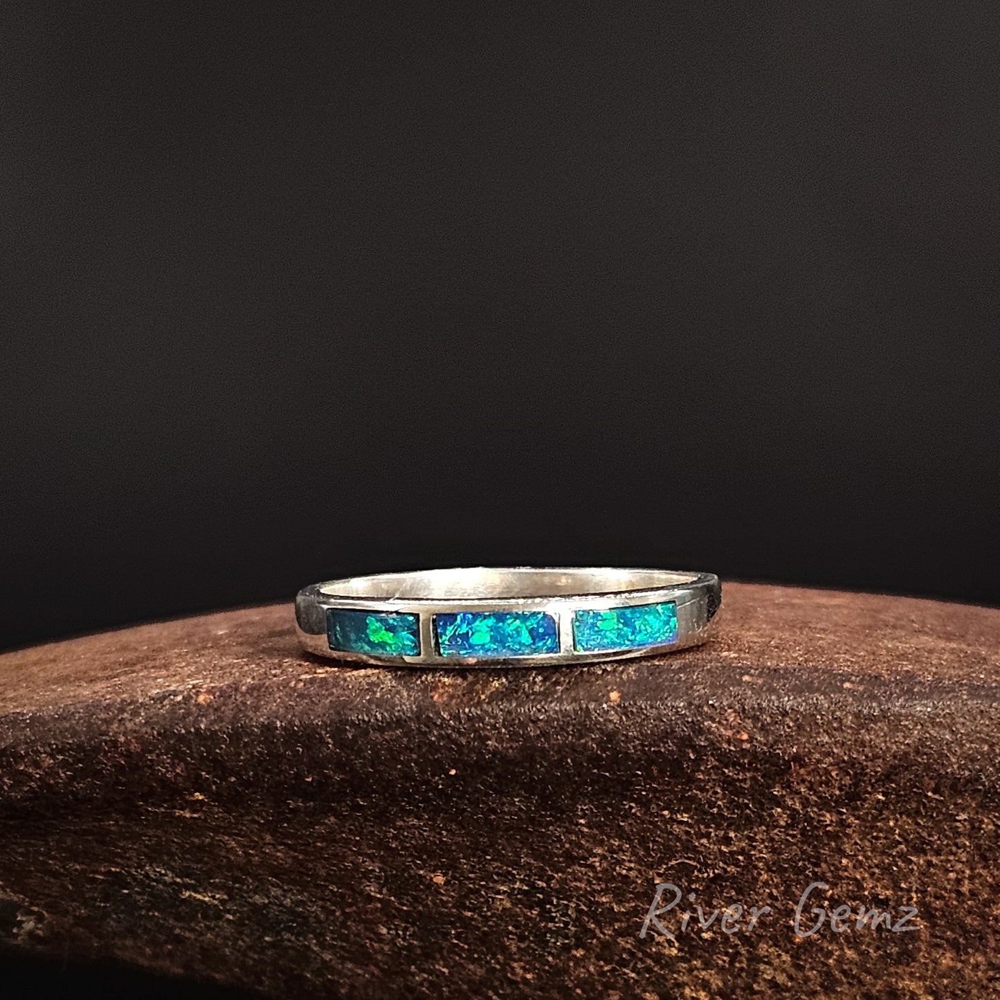 Silver ring with 3 blue & green inlayed opal stones on a dark background