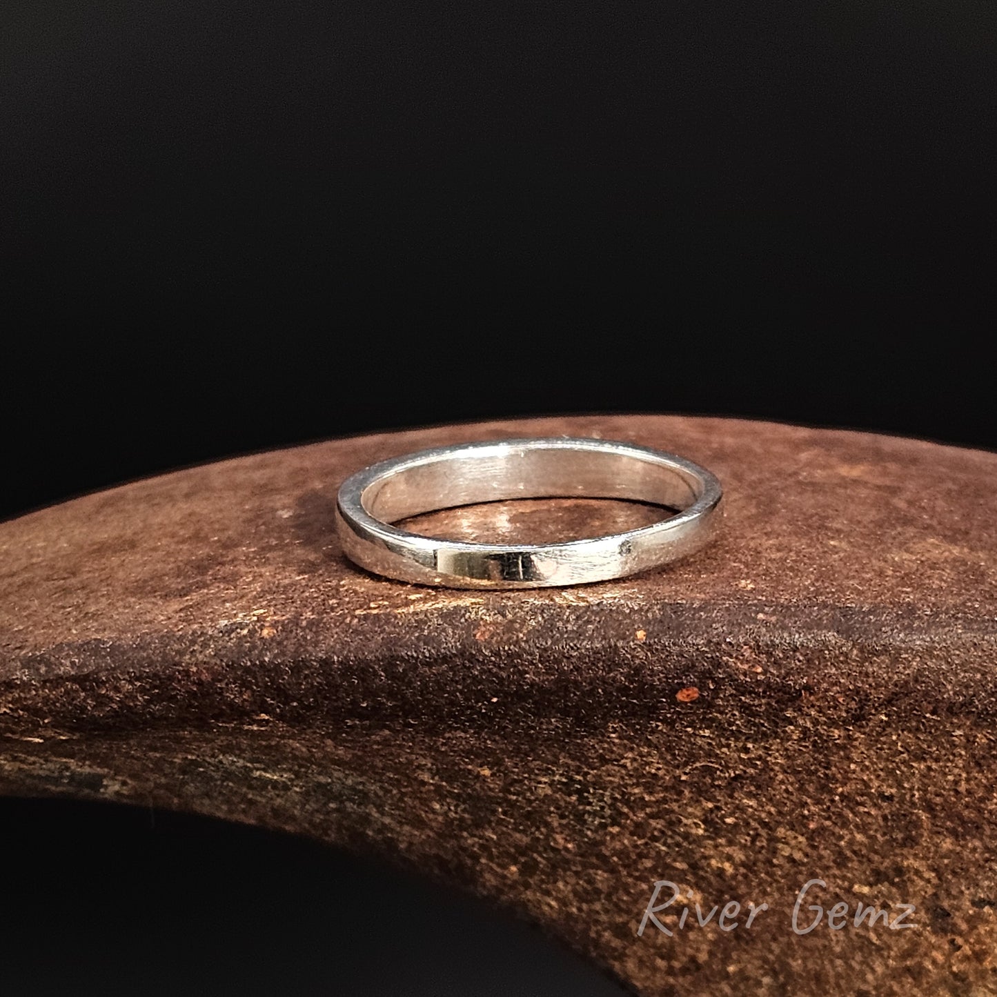 Silver ring on a dark stone surface with 'River Gene' branding.