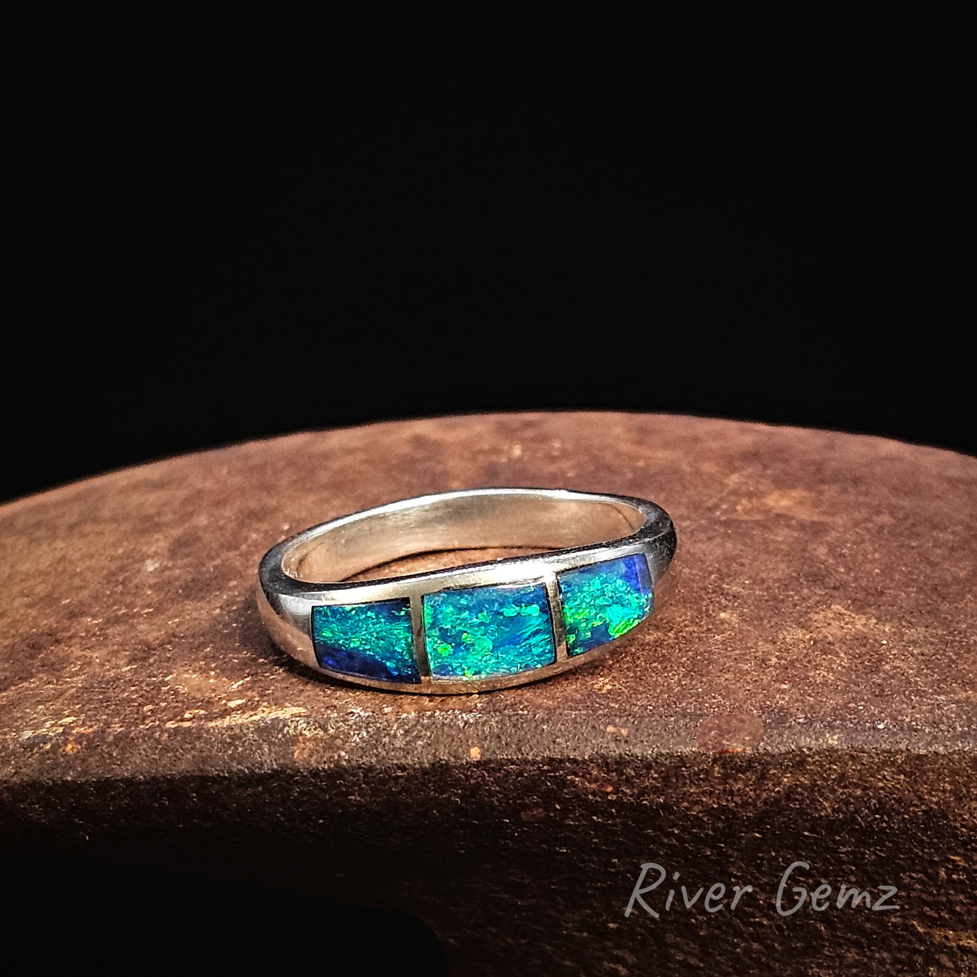 Silver ring with blue opal stones on a dark surface, branded 'River Gemz'.