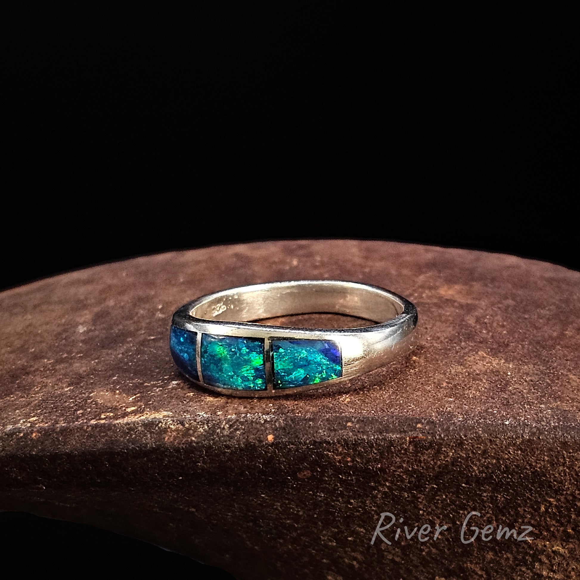 Silver ring with three inlayed blue and green opals on a dark background