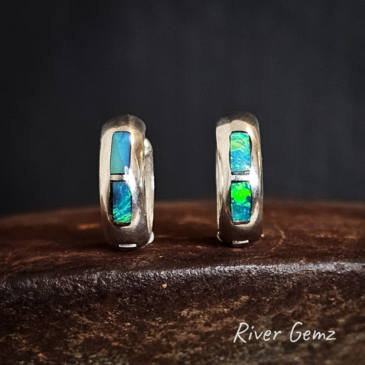 Pair of silver hoop earrings with opal inlay on a dark surface, branded 'River Gemz'.