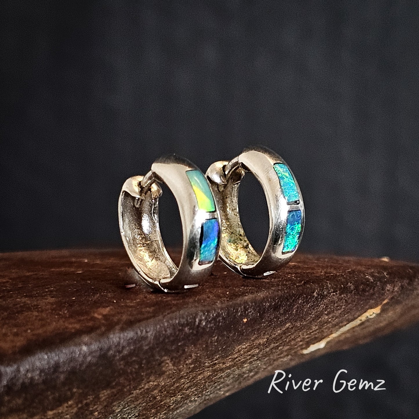 Silver huggie earrings with colorful stones on a dark background, branded 'River Gemz'.