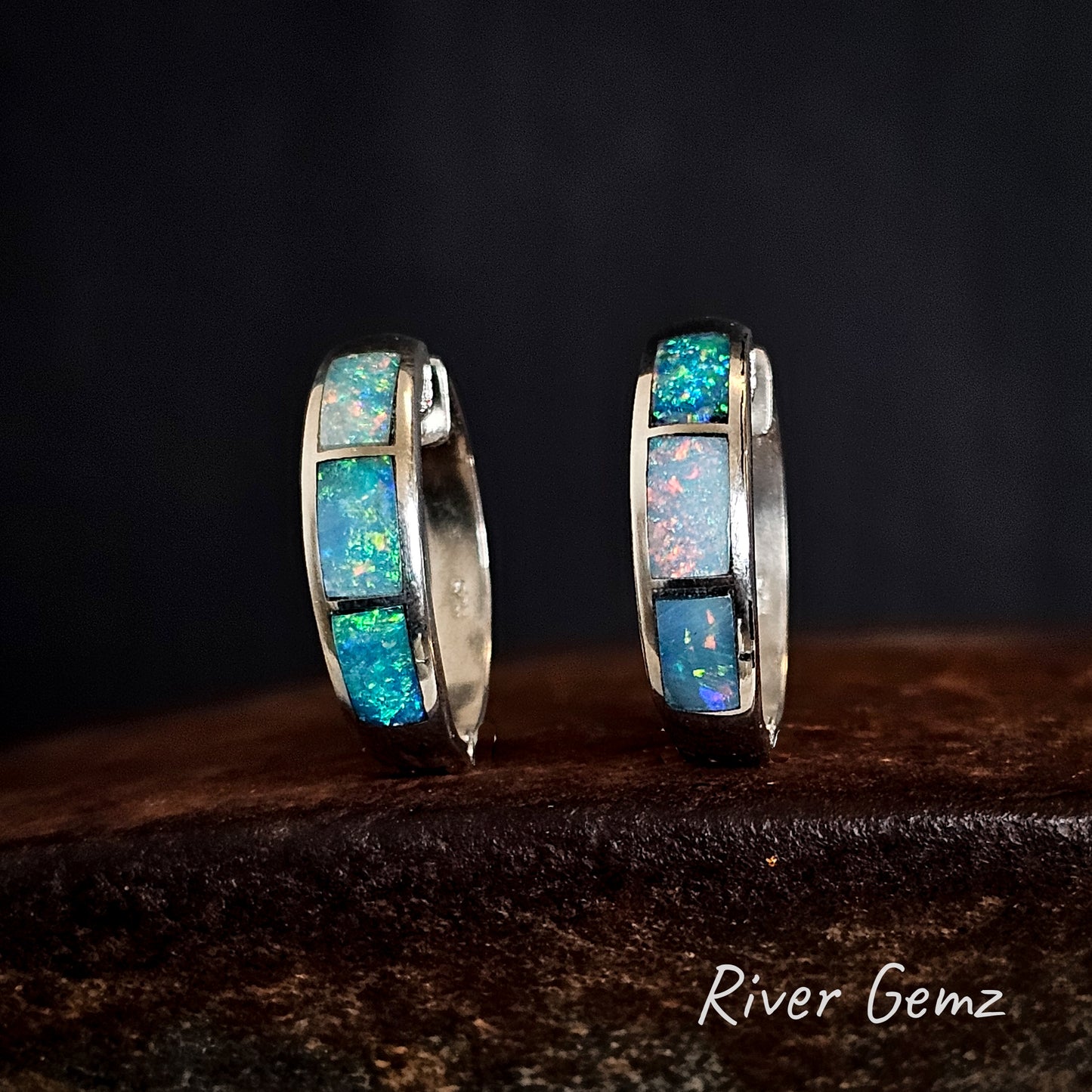 Pair of silver hoop earrings with 3 multi-coloured opals on a dark background with 'River Gemz' branding.