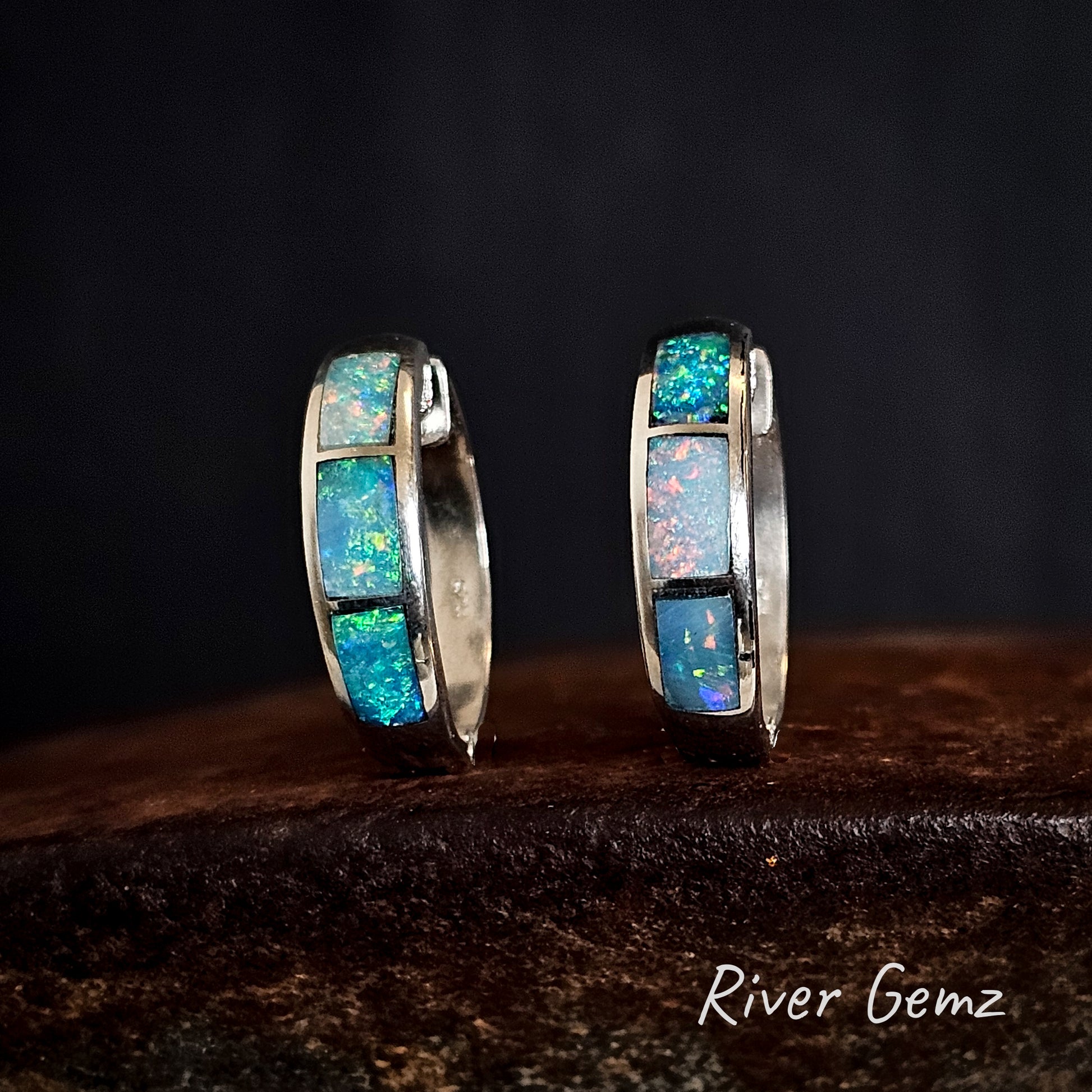 Pair of silver hoop earrings with 3 multi-coloured opals on a dark background with 'River Gemz' branding.
