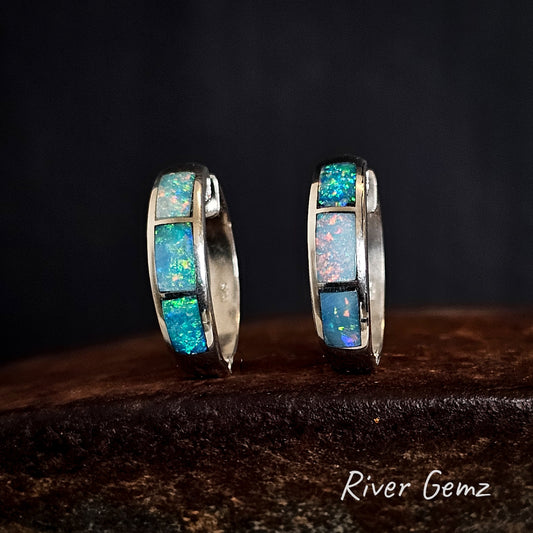 Pair of silver hoop earrings with 3 multi-coloured opals on a dark background with 'River Gemz' branding.