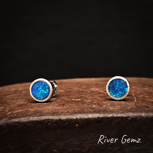 Round blue crystal opal stud earrings on a cast iron surface with 'River Gemz' branding.