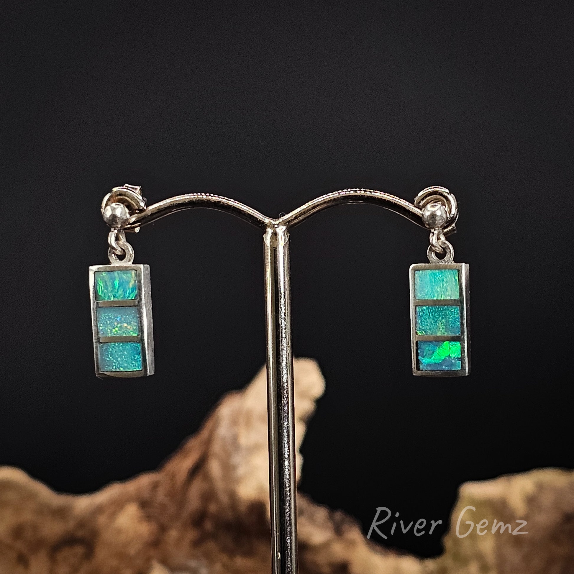 Sterling silver dangle earrings with 3 blue and green opals on a dark background.