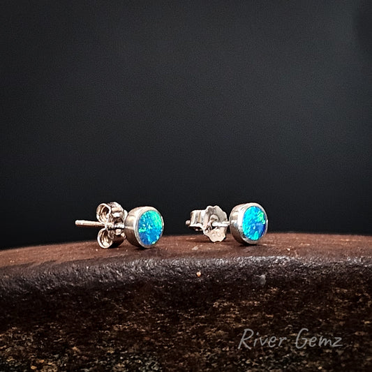 Silver stud earrings with blue gemstones on a dark background, branded 'River Gemz'.