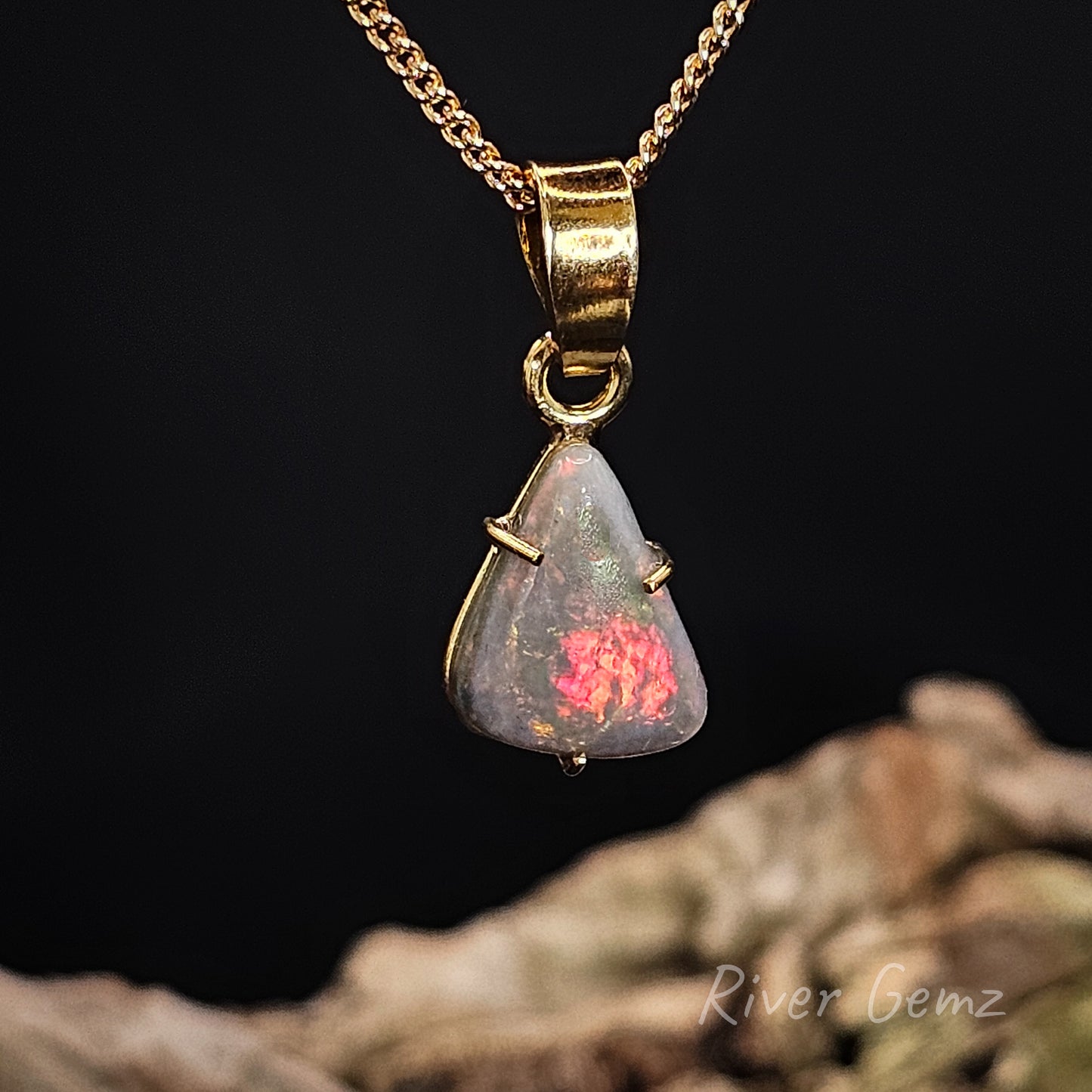 Triangular shaped dark opal claw set in yellow gold necklace on a dark background.