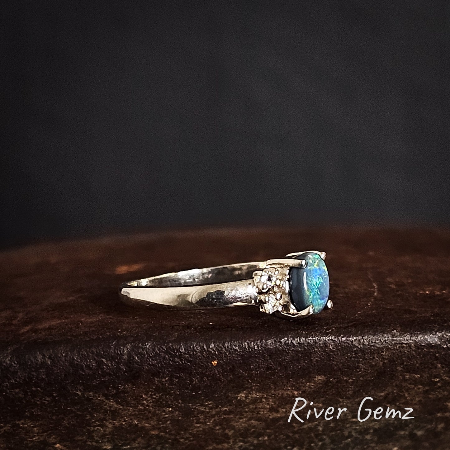 Side view of silver ring with an opal showing the thickness of the opal on a cast iron shoe anvil, branded 'River Gemz'.
