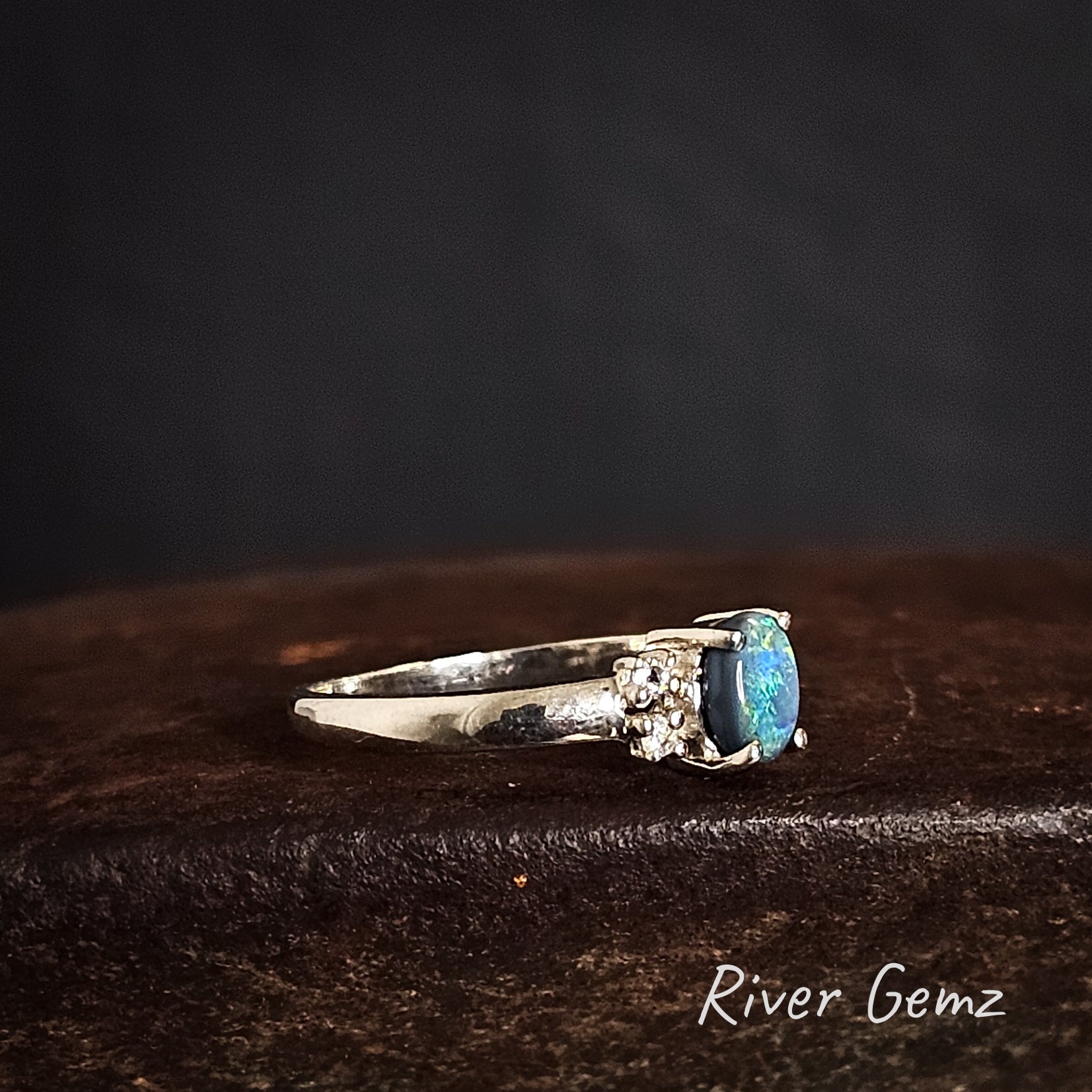 Side view of silver ring with an opal showing the thickness of the opal on a cast iron shoe anvil, branded 'River Gemz'.
