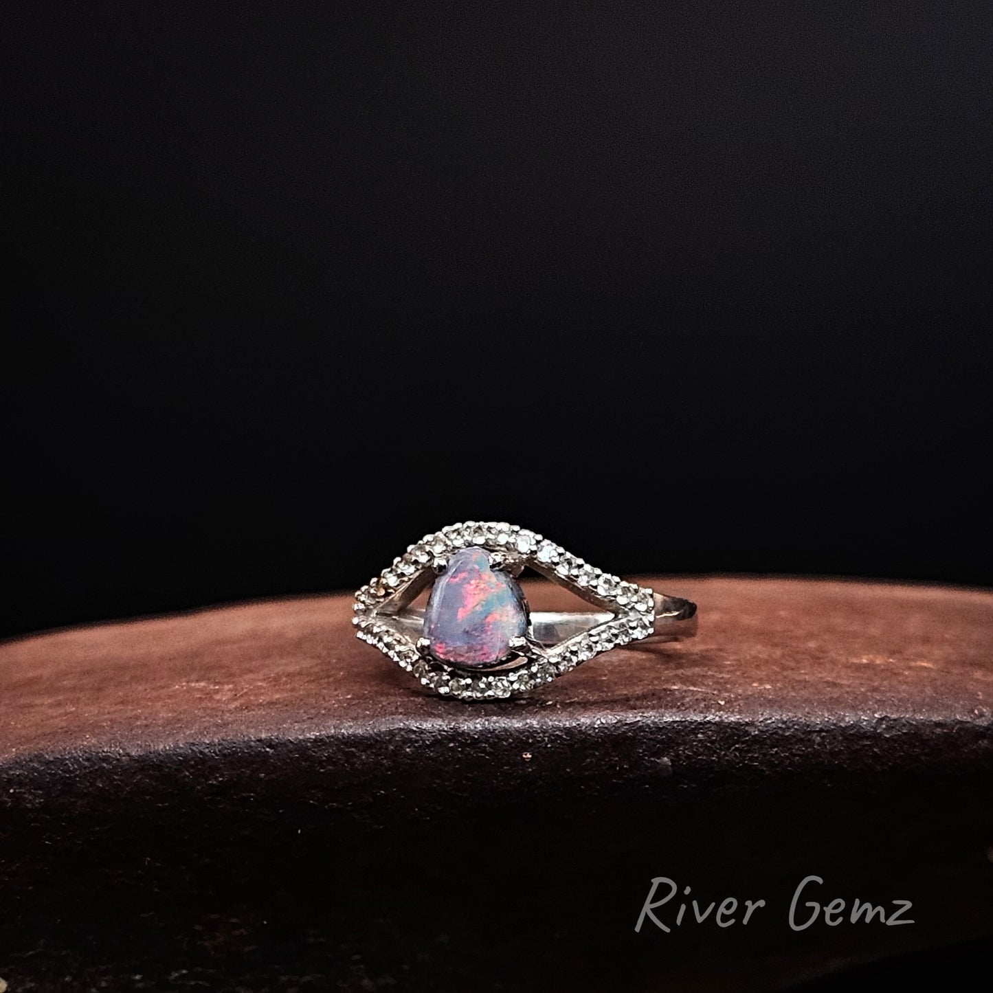 Fiery red dark opal surrounded by an eye shaped line of white topaz stones set in silver ring.