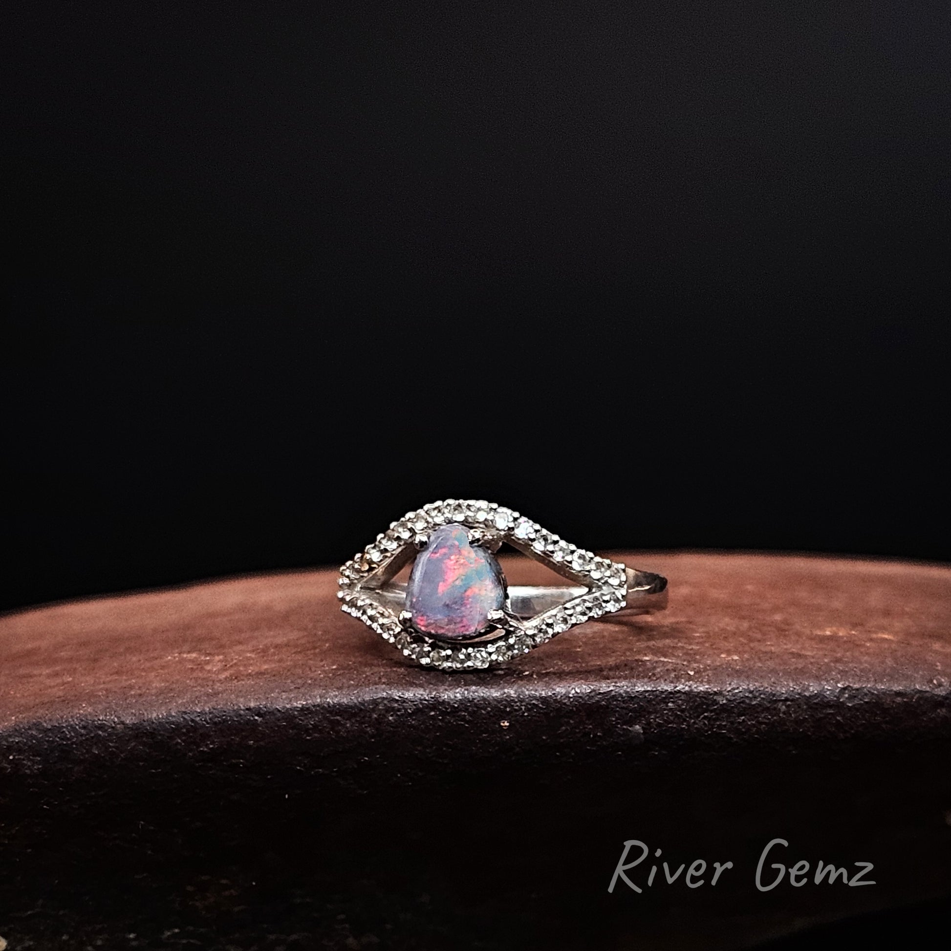 Fiery red dark opal surrounded by an eye shaped line of white topaz stones set in silver ring.