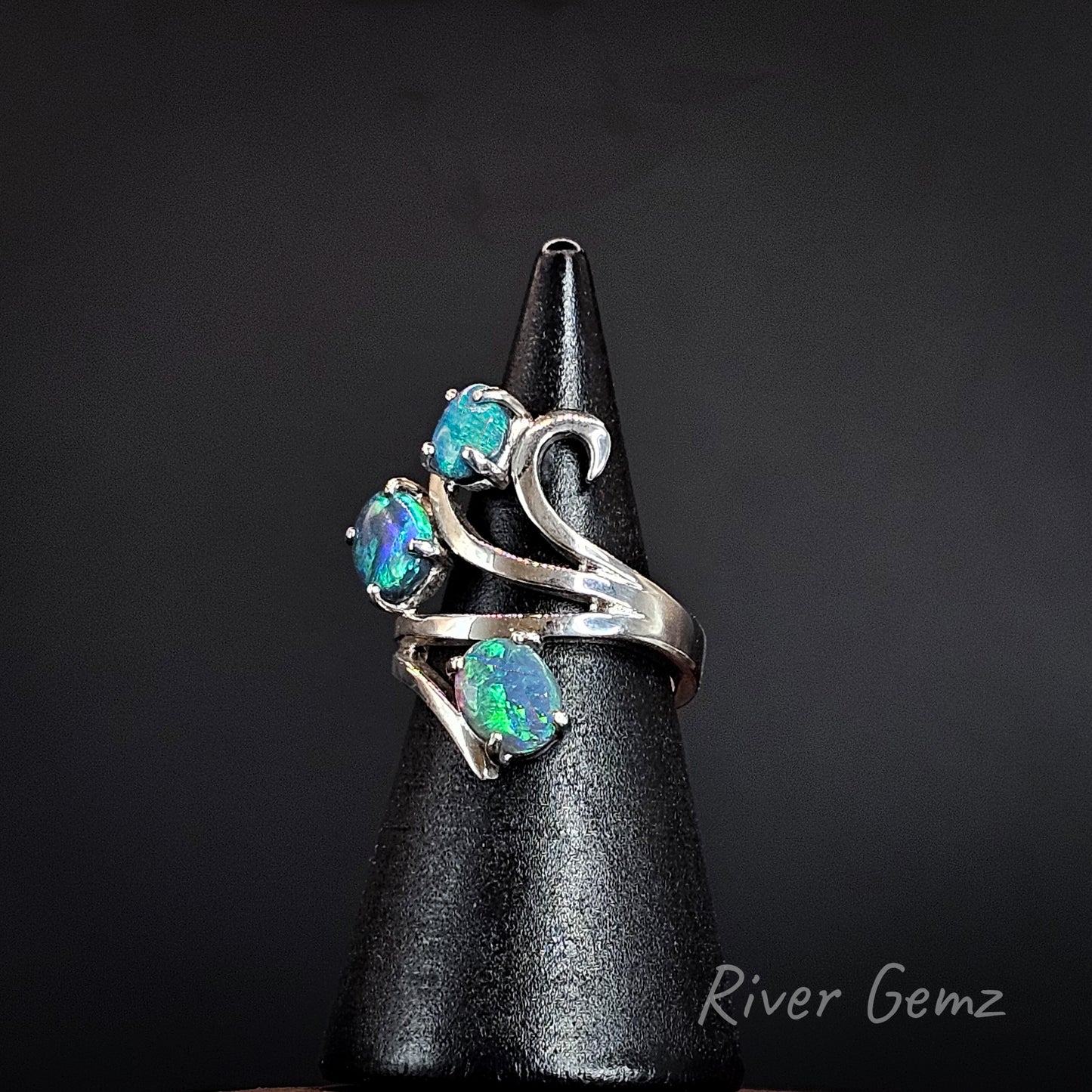 3 oval shaped blue and green opals claw set in silver ring on a black ring display cone.