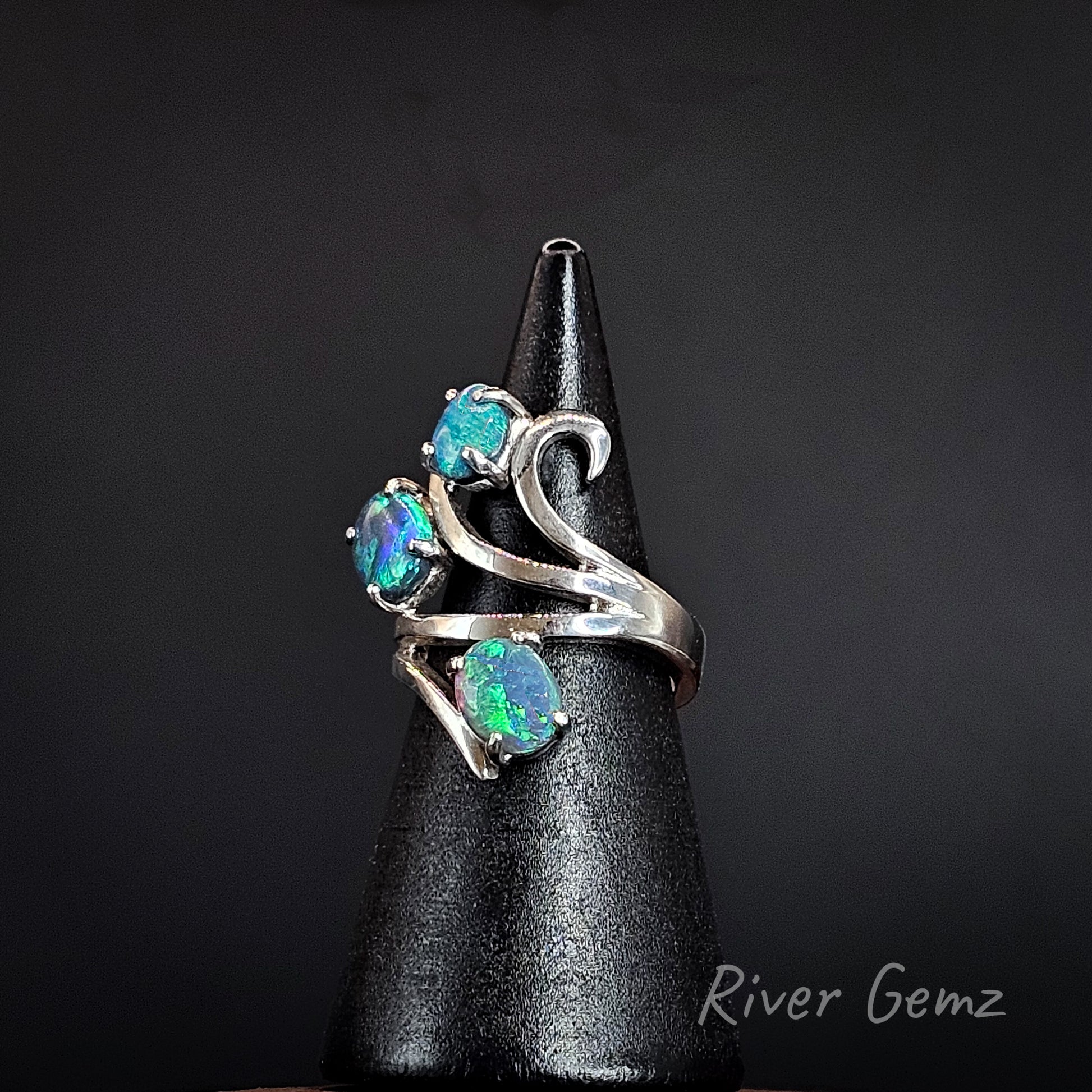 3 oval shaped blue and green opals claw set in silver ring on a black ring display cone.