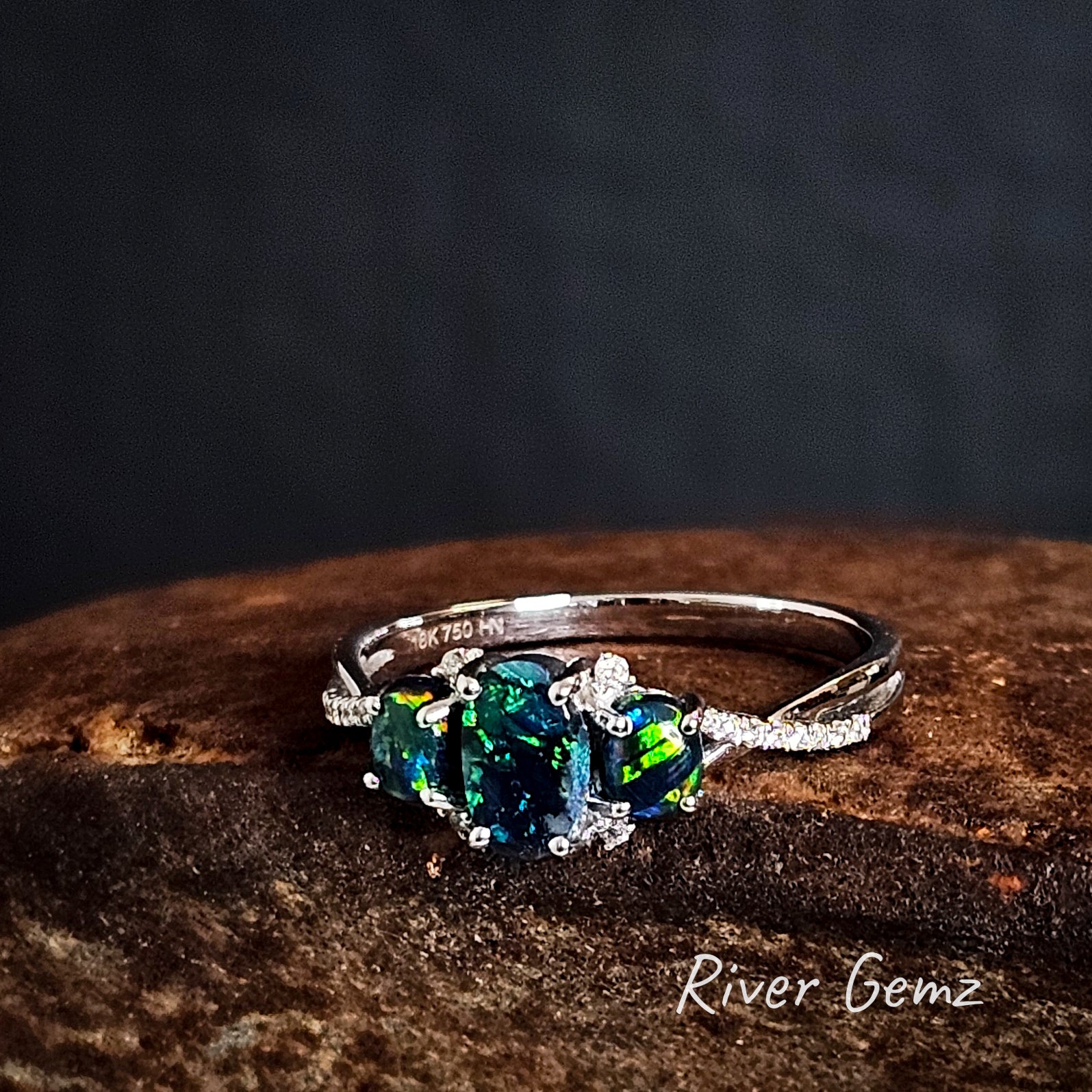 Three dark calibrated opals claw set in a white gold ring with multiple diamonds each side of the line of opals.