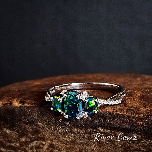 Three dark calibrated opals claw set in a white gold ring with multiple diamonds each side of the line of opals.