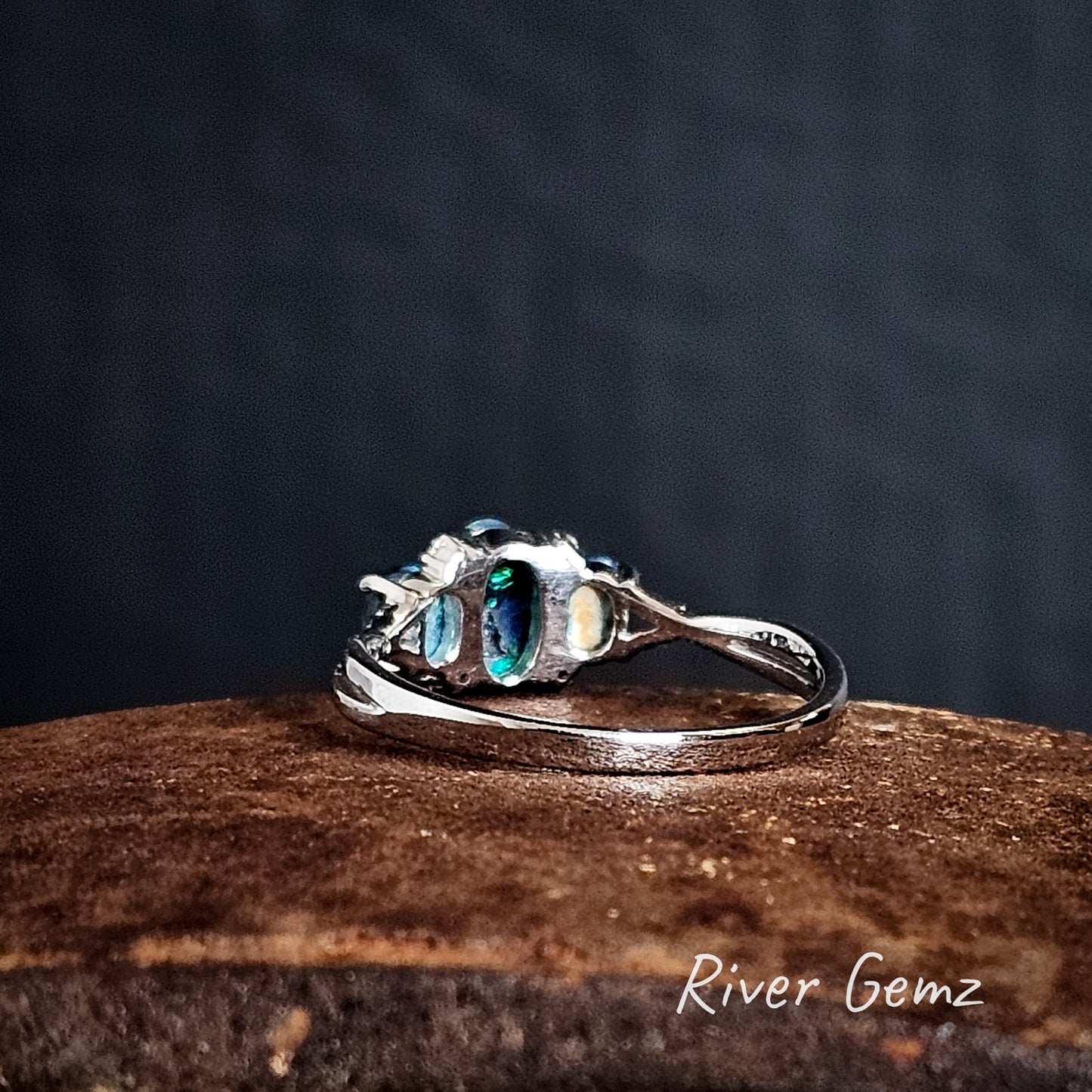 Back of silver ring showing the dark base of the black opals, featuring the brand 'River Gemz'.