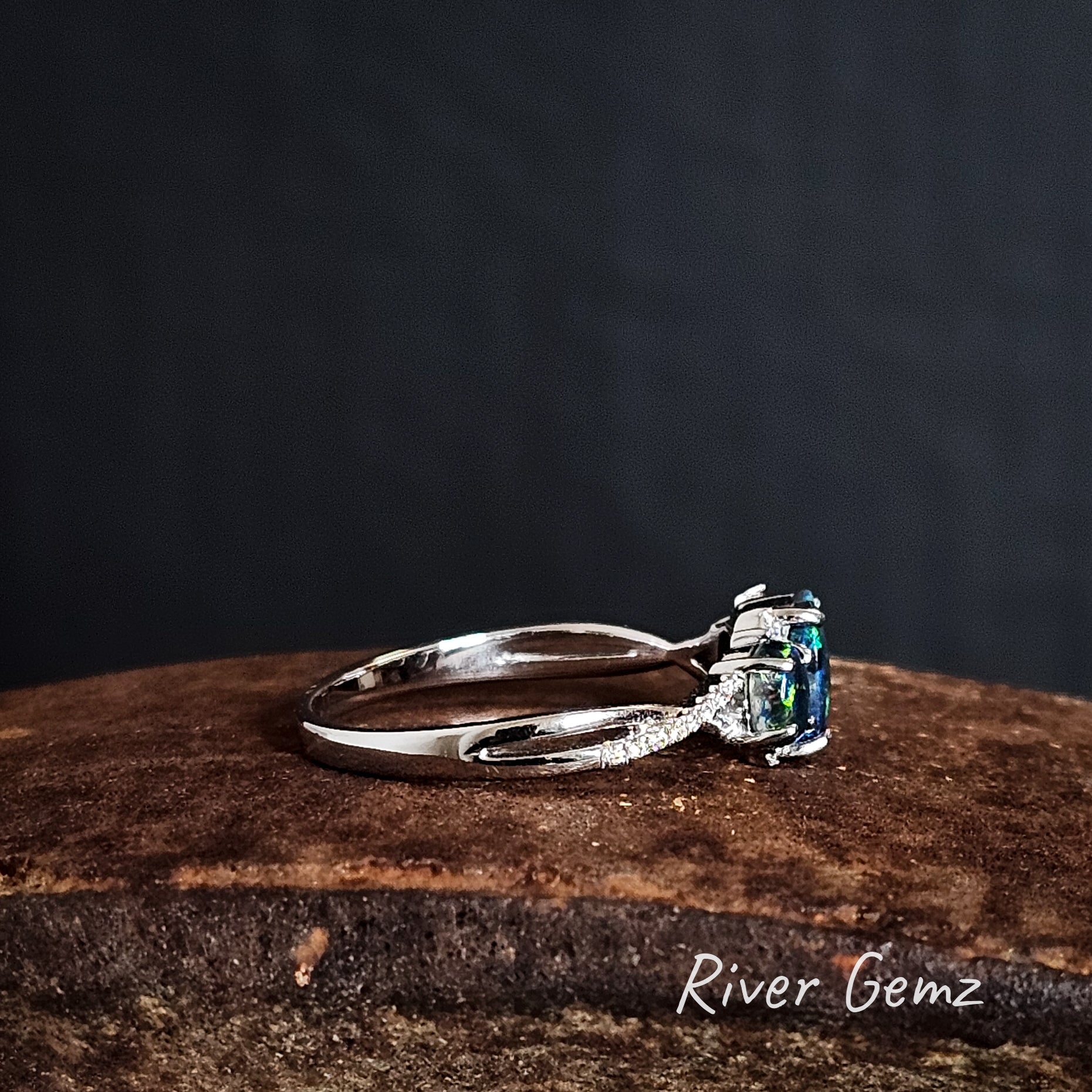 Side view of silver ring with a green black opal on a iron shoe anvil with a dark background