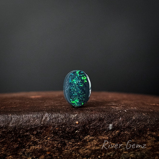 Oval shaped black opal stone on a dark surface with a black background