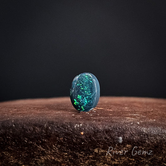 Green coloured loose black opal on a dark background with 'River Gemz' branding.