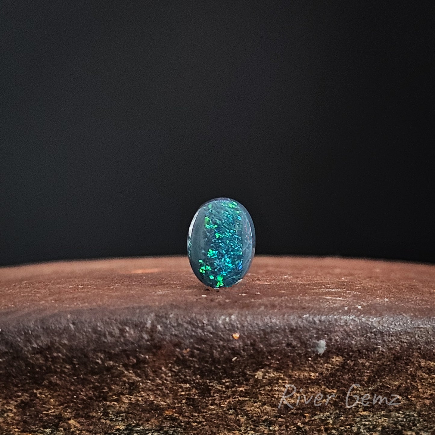 Oval shaped blue-green black opal on a dark background