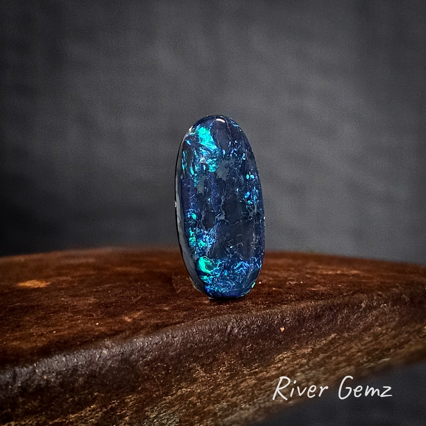 Blue oval shaped black opal on a cast iron surface with 'River Gemz' branding.
