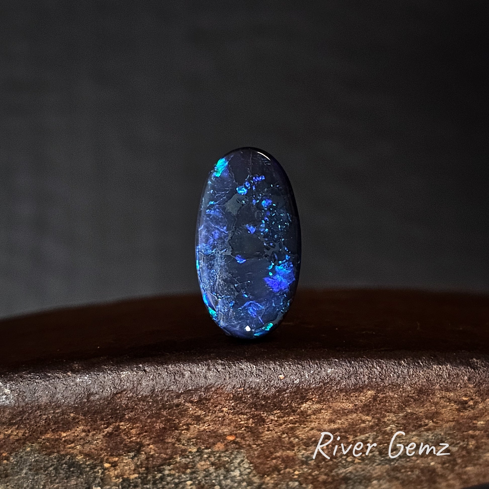 Blue, purple and green black opal stone on a dark background with 'River Gemz' branding.