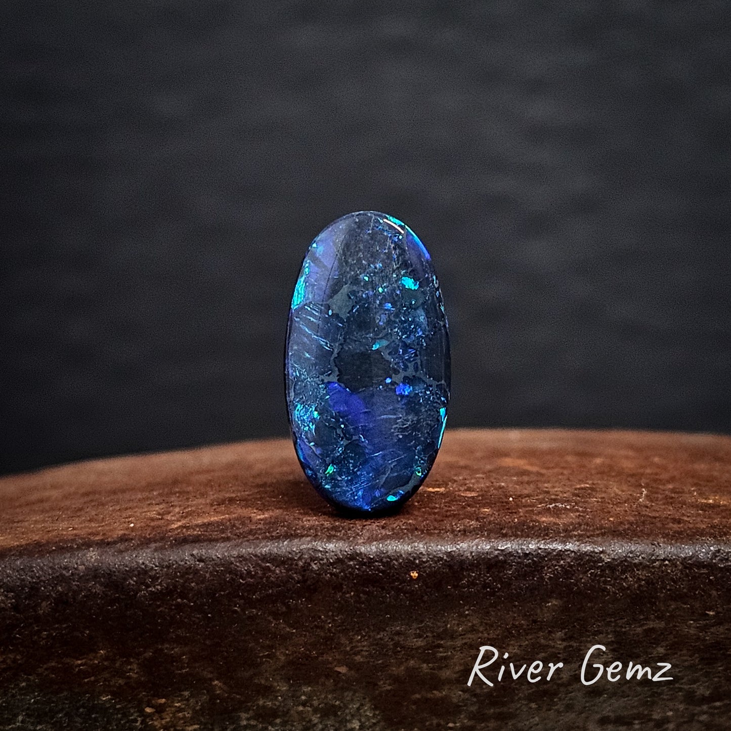 Blue oval shaped black opal on a dark background with 'River Gemz' branding.