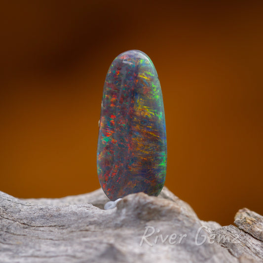 Colourful oval shaped opal shown erect on light grey grained piece of driftwood.