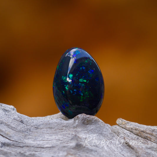 High domed cut opal with spheres of blue and green throughout this high quality opal. The opal is standing upright on a light-grey grained piece of driftwood.