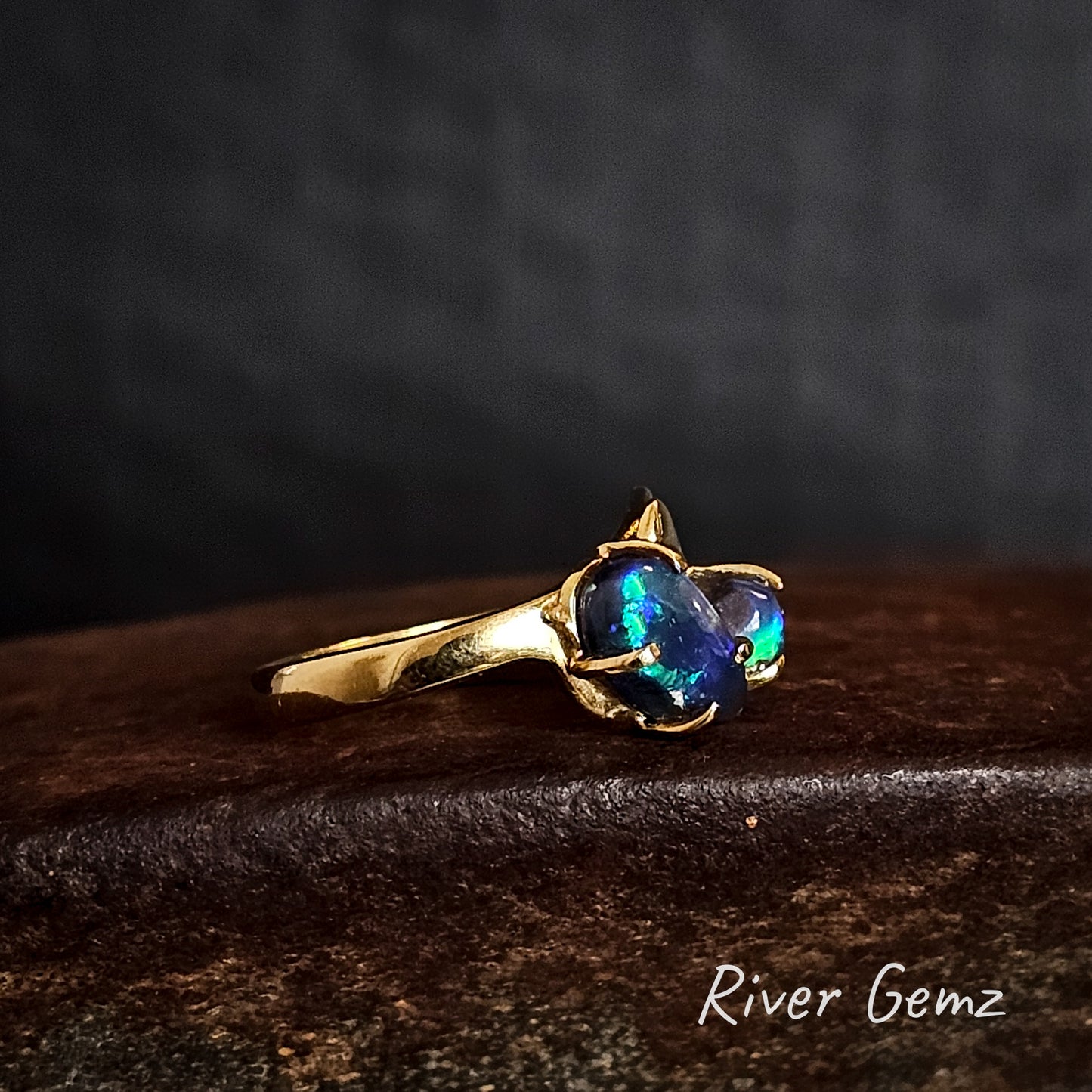 Two dark blue and green black opals claw set in a yellow gold ring.