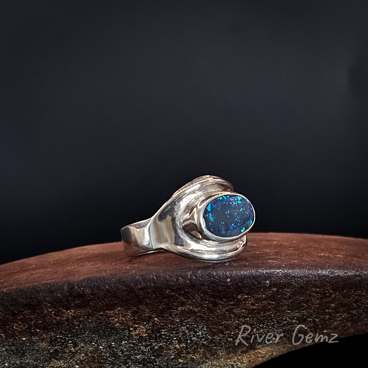 Dark opal fully bezel set in large men's silver ring on an ironstone shoe anvil and black background.
