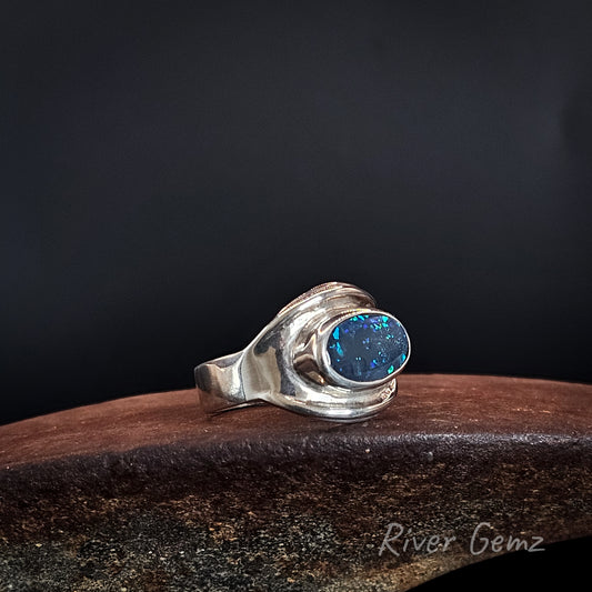 Dark opal fully bezel set in large men's silver ring on an ironstone shoe anvil and black background.