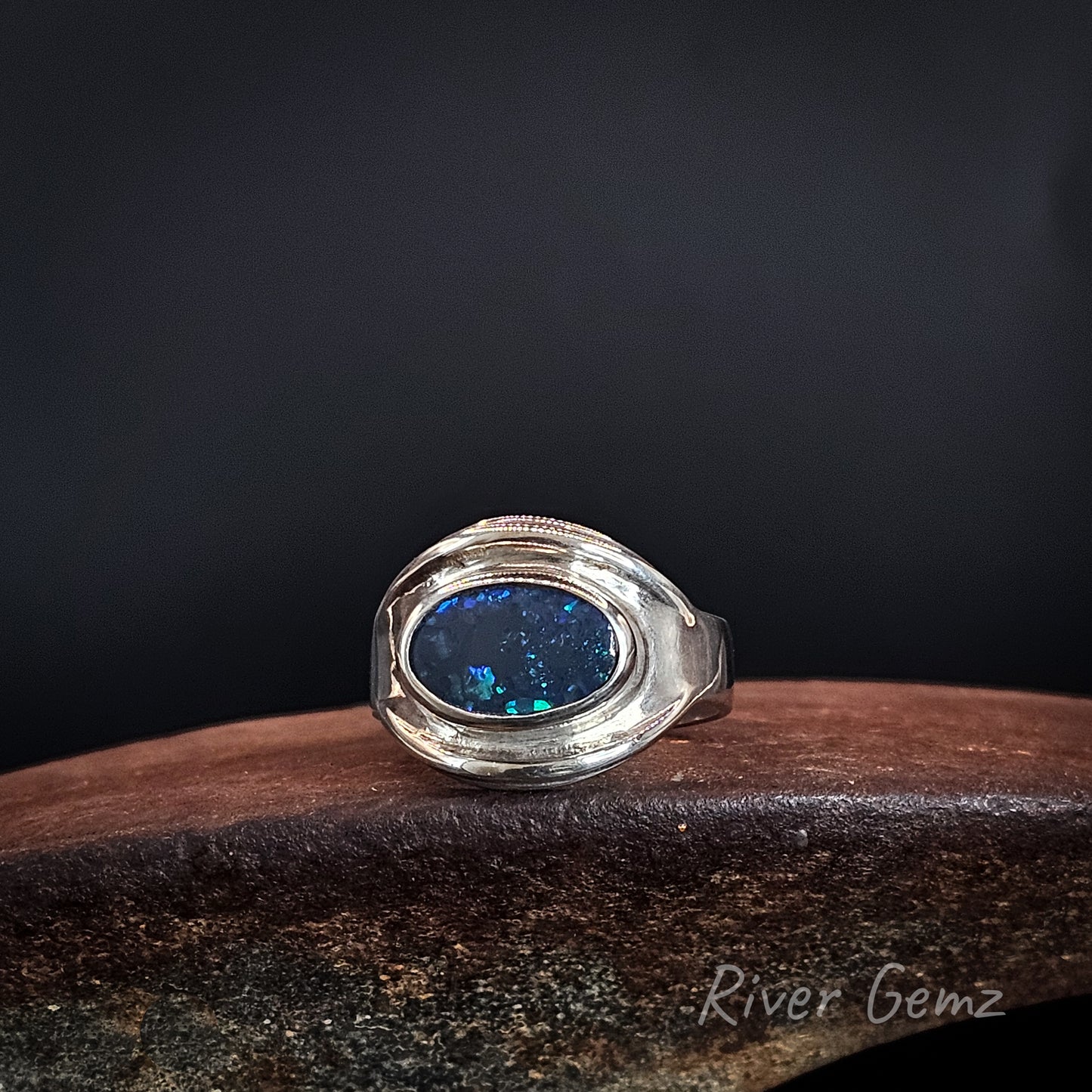 Oval shaped blue and green black opal set East-West in a silver ring.