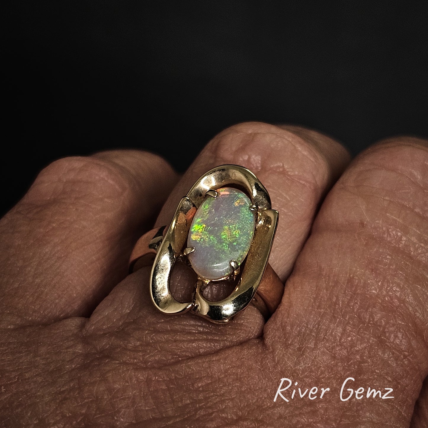 Gold ring with an opal stone on a hand, branded 'River Gemz'.