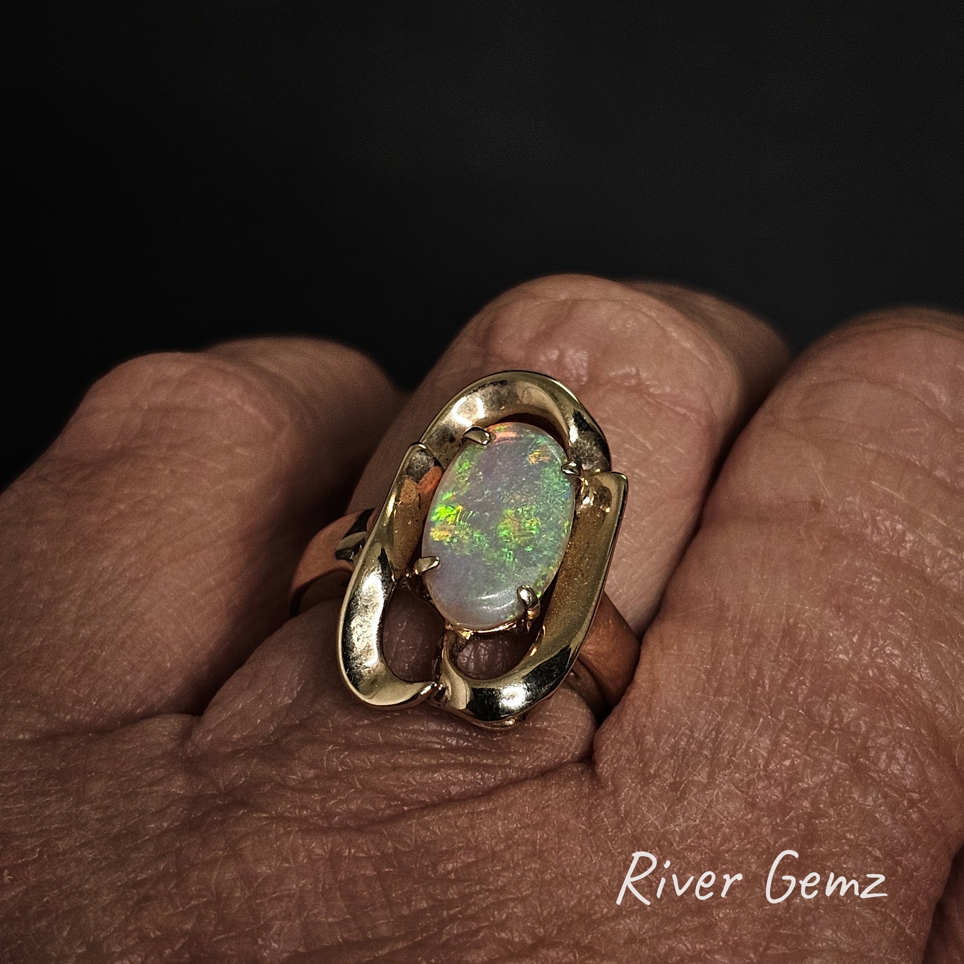 Gold ring with an opal stone on a hand, branded 'River Gemz'.