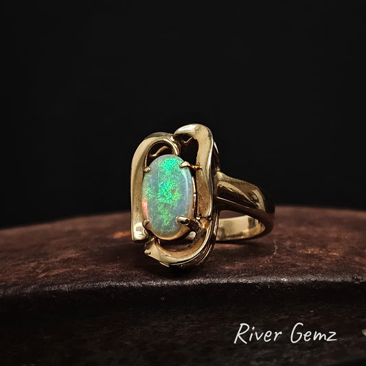 Yellow gold ring with an oval shaped green opal on a dark background, branded 'River Gemz'.