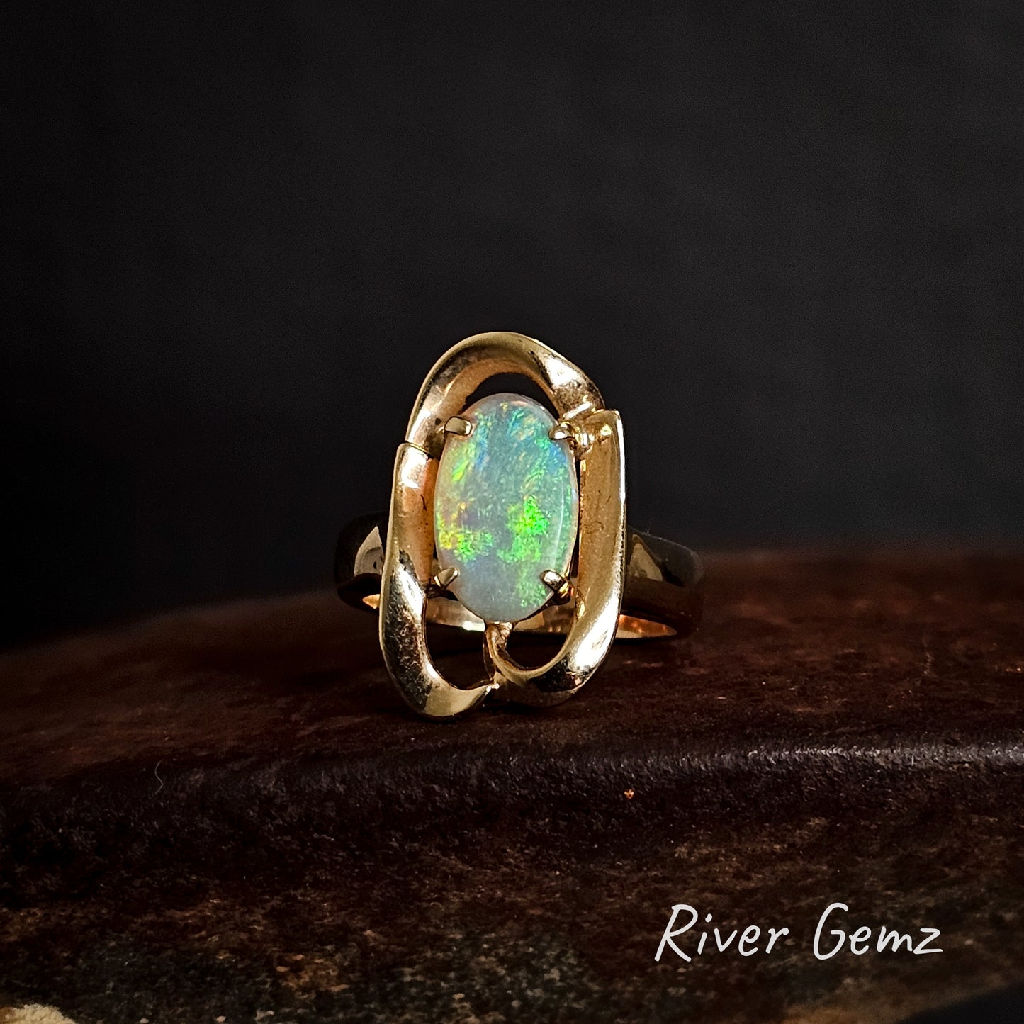 Crystal opal claw set in 14K gold ring on a dark background, branded 'River Gemz'.