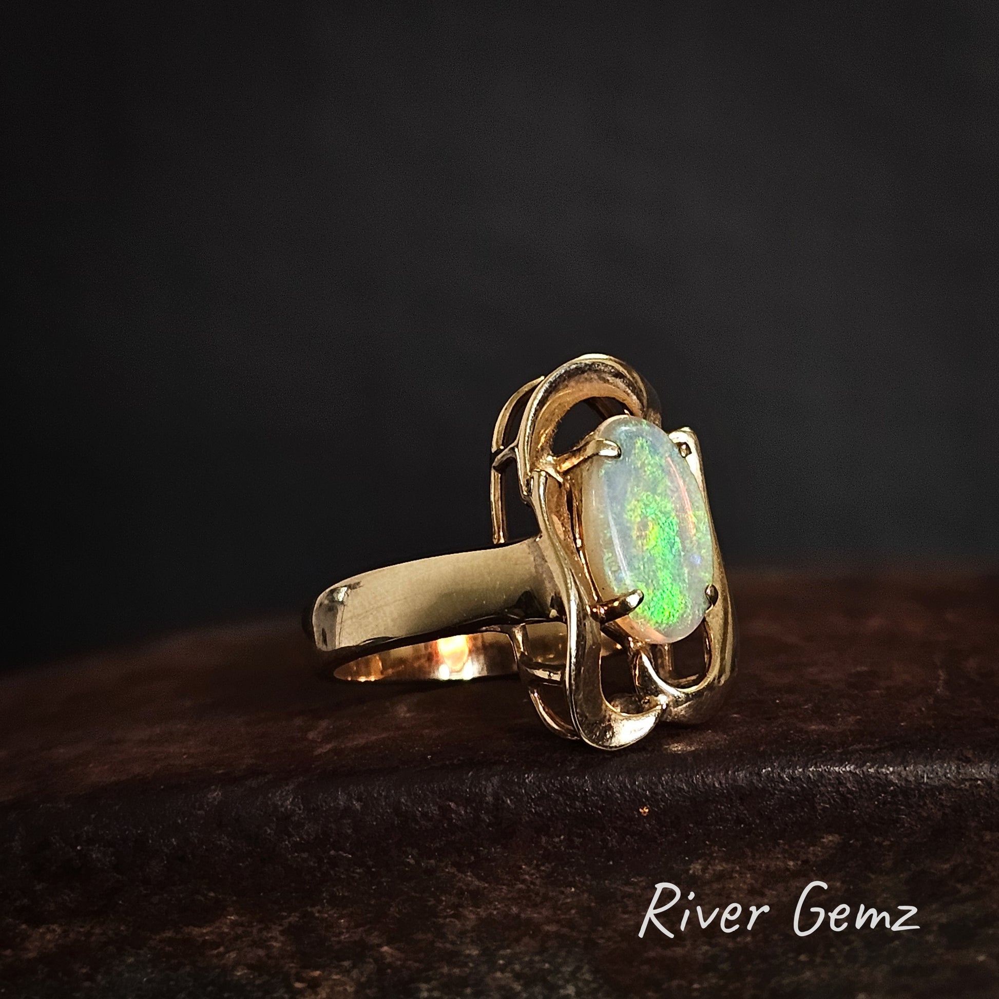 Side view of gold & opal ring showing the wide and uniform band on a dark background, branded 'River Gemz'.