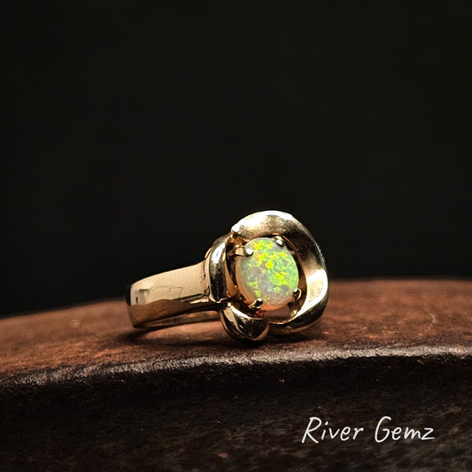 Gold ring with an opal stone on a dark surface, branded 'River Gemz'.