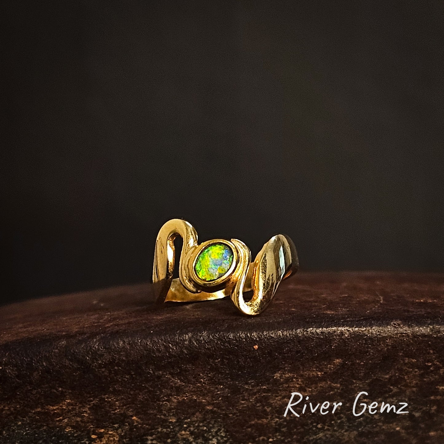 Gold ring with a green gemstone on a dark background, branded 'River Gemz'.