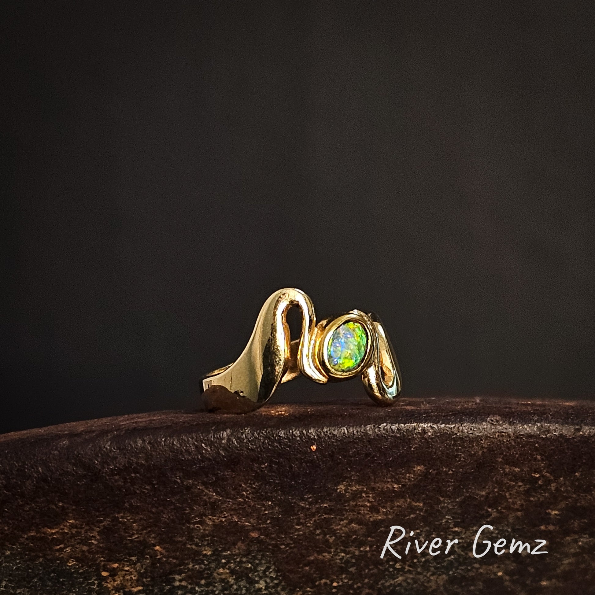 Gold wave style ring with a green opal on a dark background, featuring the brand 'River Gemz'.